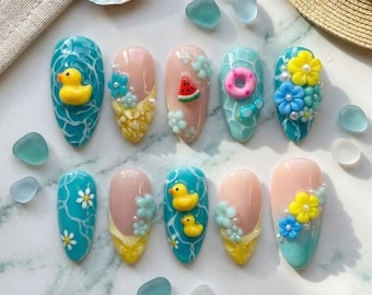 May include: A set of ten almond-shaped artificial nails with summer-themed designs. The nails feature various designs, including a yellow rubber duck, watermelon slices, and floral accents. Colors include blue, pink, yellow, and white.