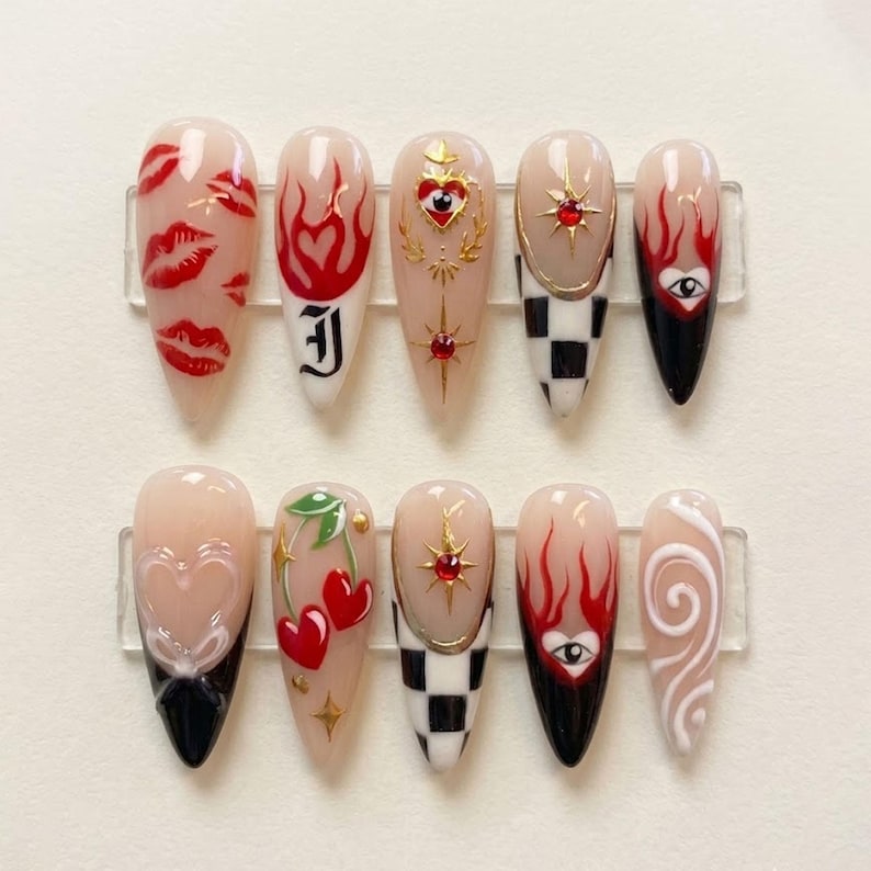May include: A set of ten long, almond-shaped artificial nails with various designs. The designs include red lips, flames, hearts, cherries, and a checkerboard pattern. Some nails feature gold accents and a black base.