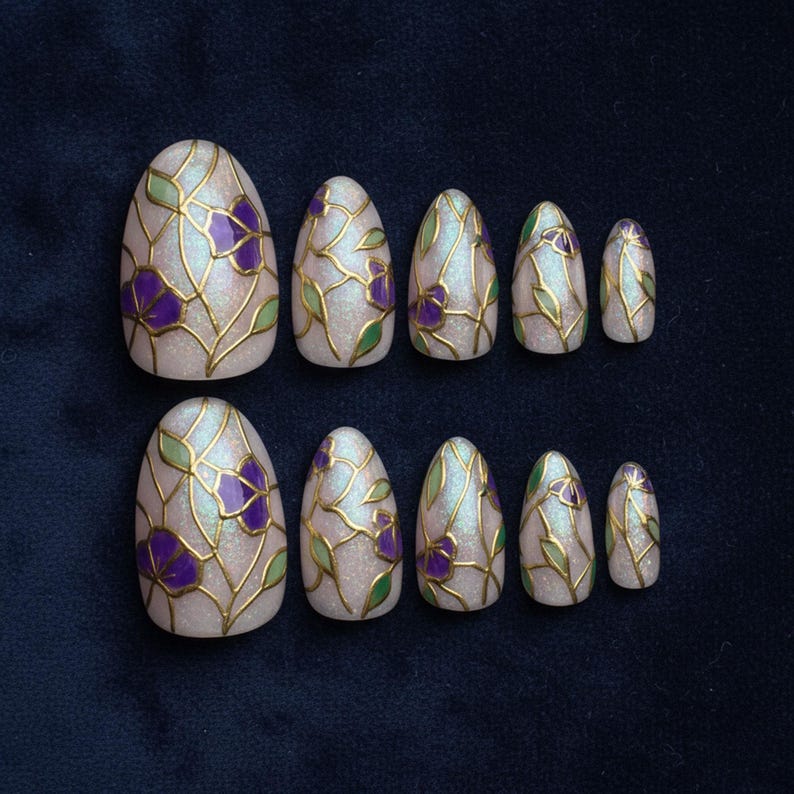May include: Set of ten oval-shaped press-on nails. Each nail is painted with a pearlescent base, gold outlines, and purple flower and green leaf designs. The nails are arranged on a dark blue surface.