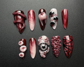 May include: A collection of ten artificial nails in dark red and white. The nail art includes designs such as a tentacle, a tooth, an eyeball, and a spiderweb, ideal for a Halloween look.