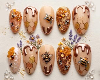 Puede incluir: Un conjunto de diez uñas artificiales en forma de almendra con temática de abeja. Las uñas presentan una base nude con purpurina dorada, diseños de goteo de miel, patrones de panal y adornos 3D de abejas y flores.