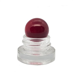 May include: A clear glass bottle stopper featuring a smooth, spherical dark red glass top. The base of the stopper is made of transparent glass with visible screw threads designed for a secure fit into a corresponding bottle opening.
