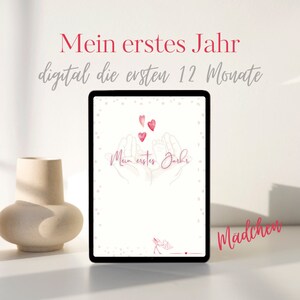 May include: A digital baby journal cover with a pink background and white polka dots. The cover features two hands holding a baby's foot with three pink hearts floating above. The text "Mein erstes Jahr" and "digital die ersten 12 Monate" is displayed at the top of the cover. The text "Mädchen" is displayed at the bottom of the cover.
