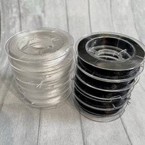 May include: Two spools of clear elastic string, one white and one black, in plastic containers.