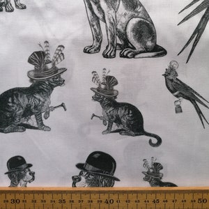 May include: A white fabric with a repeating pattern of black and white illustrations of a dog, cat, and bird wearing hats. The dog and cat are holding a walking stick. The bird is perched on a bell.