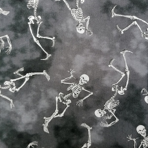May include: Black and white fabric with a repeating pattern of skeletons dancing on a grey background. The fabric is measured with a ruler in inches.