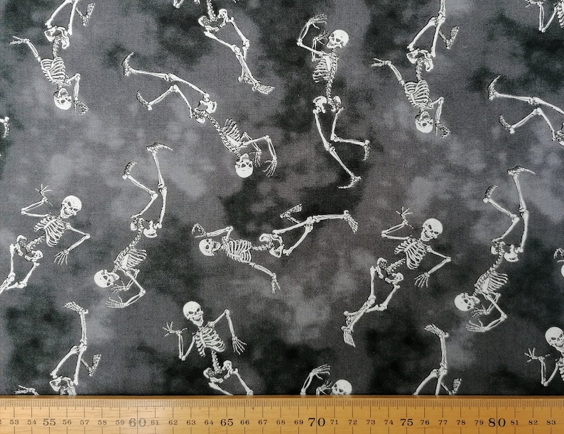 May include: A black and white fabric with a repeating pattern of skeletons dancing. The skeletons are white against a dark grey background.
