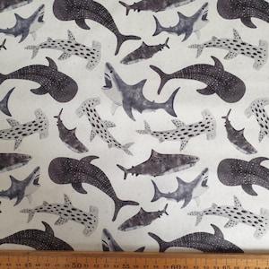 May include: A white fabric with a repeating pattern of black and grey sharks and hammerhead sharks. The sharks are in various sizes and positions, some facing left and some facing right.