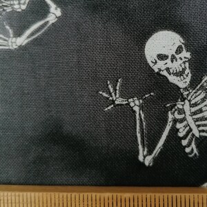 May include: Black fabric with a white skeleton design. The skeleton is waving with a toothy grin. A ruler is in the bottom of the image with the numbers 80, 81, 82, 83, and 84 visible.