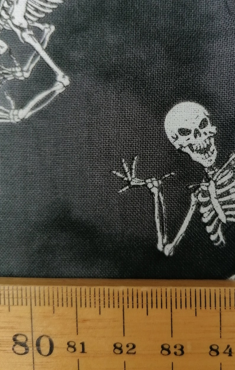 May include: Black fabric with a white skeleton design. The skeleton is waving with a toothy grin. A ruler is in the bottom of the image with the numbers 80, 81, 82, 83, and 84 visible.