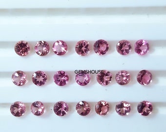 Puede incluir: Veinticuatro piedras preciosas redondas de color rosa dispuestas en tres filas sobre una superficie blanca. Las piedras preciosas son todas de tamaño y forma aproximadamente iguales. El texto "GEMSHouse" está impreso en la superficie.