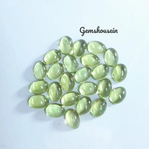 May include: A collection of oval-shaped, pale green gemstones. The gems are arranged in a cluster, each with a smooth, polished surface. The background is a plain white, with the text "Gemshousein" in cursive script.