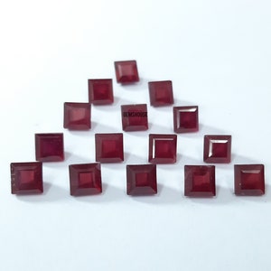 May include: Arrangement of square-cut, deep red gemstones. The gems are arranged on a white surface. The text "GEMSHOUSE" is visible on the surface. The gemstones are a rich, saturated color.
