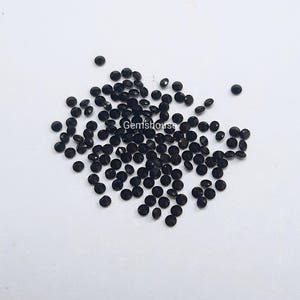 May include: A large quantity of small, round, black gemstones. The gemstones are scattered on a white surface.