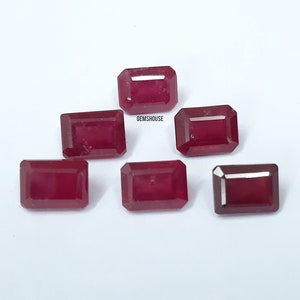 May include: Six red ruby gemstones in an emerald cut. The gemstones are arranged in two rows of three. The gemstones are on a white background. GEMSHouse is printed on the background.