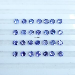 Pu&ograve; includere: Ventiquattro gemme rotonde, sfaccettate, di colore blu chiaro disposte in tre file da otto su una superficie bianca. GEMSHOUUSE &egrave; stampato in nero sotto le gemme.