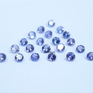 Pu&ograve; includere: Una collezione di pietre preziose rotonde, sfaccettate, di colore blu chiaro. Le pietre preziose sono sparse su una superficie bianca.