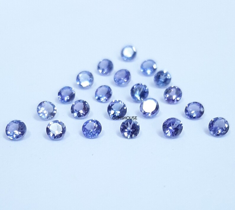 Pu&ograve; includere: Una collezione di pietre preziose rotonde, sfaccettate, di colore blu chiaro. Le pietre preziose sono sparse su una superficie bianca.