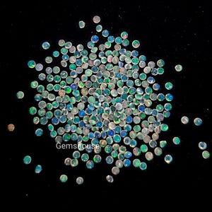 May include: A collection of small, round opals with iridescent colors of blue, green, and red, scattered on a black background. The opals have a faceted cut, and the text "Gemshouse" is visible in the center.