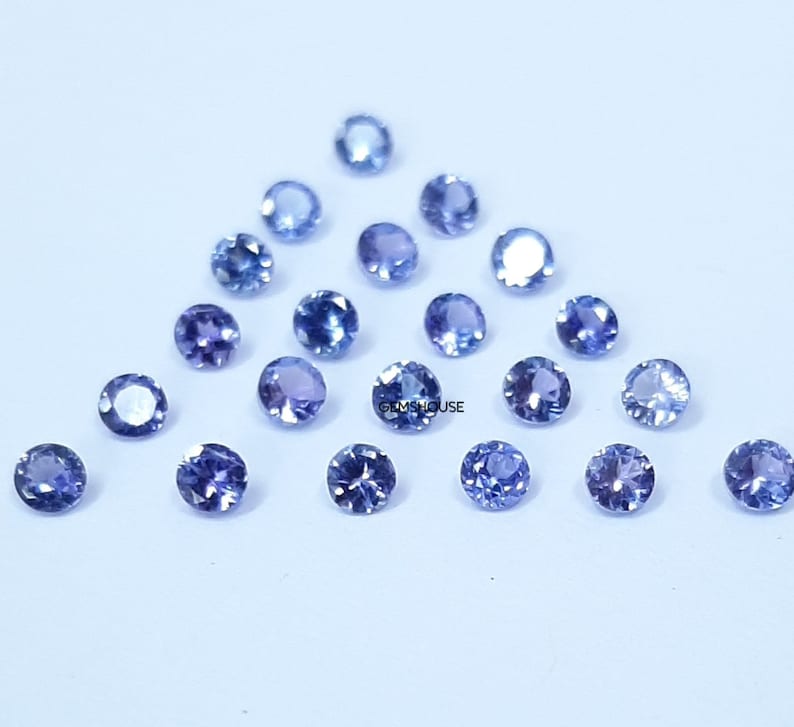 Pu&ograve; includere: Una collezione di 18 pietre preziose rotonde, sfaccettate, blu. Le pietre preziose sono sparse su una superficie bianca.
