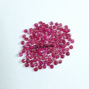 Op de afbeelding: Een stapel van ongeveer 100 kleine, ronde, gefacetteerde robijn edelstenen. De edelstenen zijn diep roze van kleur en hebben een hoge glans.