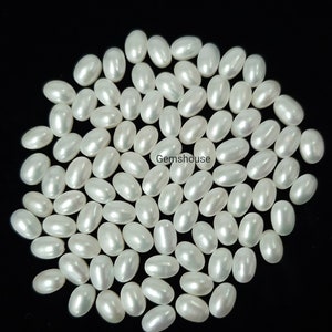 Può includere: Una collezione di circa 60 perle d'acqua dolce di forma ovale e colore bianco. Le perle sono lisce e lucide, con un leggero bagliore iridescente. Sono disposte in un cerchio sciolto su uno sfondo nero.