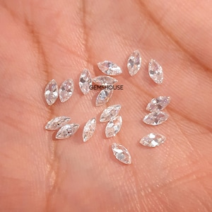 May include: A collection of marquise-cut, clear gemstones. The gemstones are scattered across a light-colored surface. The image includes the text "GEMSHOUSE".