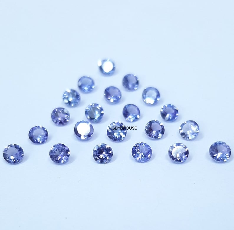 Pu&ograve; includere: Una collezione di 20 pietre preziose rotonde, sfaccettate, di colore blu chiaro. Le pietre preziose sono sparse su uno sfondo blu chiaro.