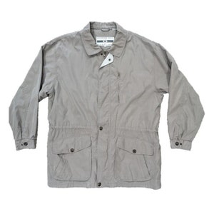 May include: A light grey Members Only jacket with a collared neckline, button closure, and multiple pockets. The jacket has long sleeves with buttoned cuffs and a drawstring waist. The jacket is made of a lightweight material.