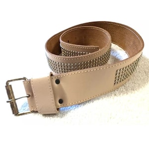 May include: A light brown leather belt with a silver studded design and a brass buckle.