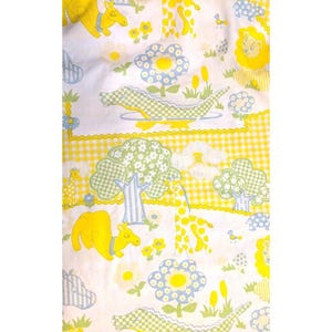 May include: A white fabric featuring a repeating pattern of yellow camels, green checkered crocodiles, and light blue flowers. The design includes yellow gingham borders, stylized green trees, and small yellow lions, creating a colorful and detailed textile surface.