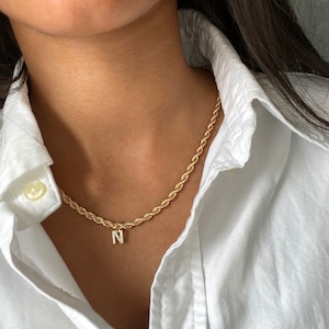May include: A gold rope chain necklace with a small pendant featuring the letter 'N' encrusted with clear rhinestones.