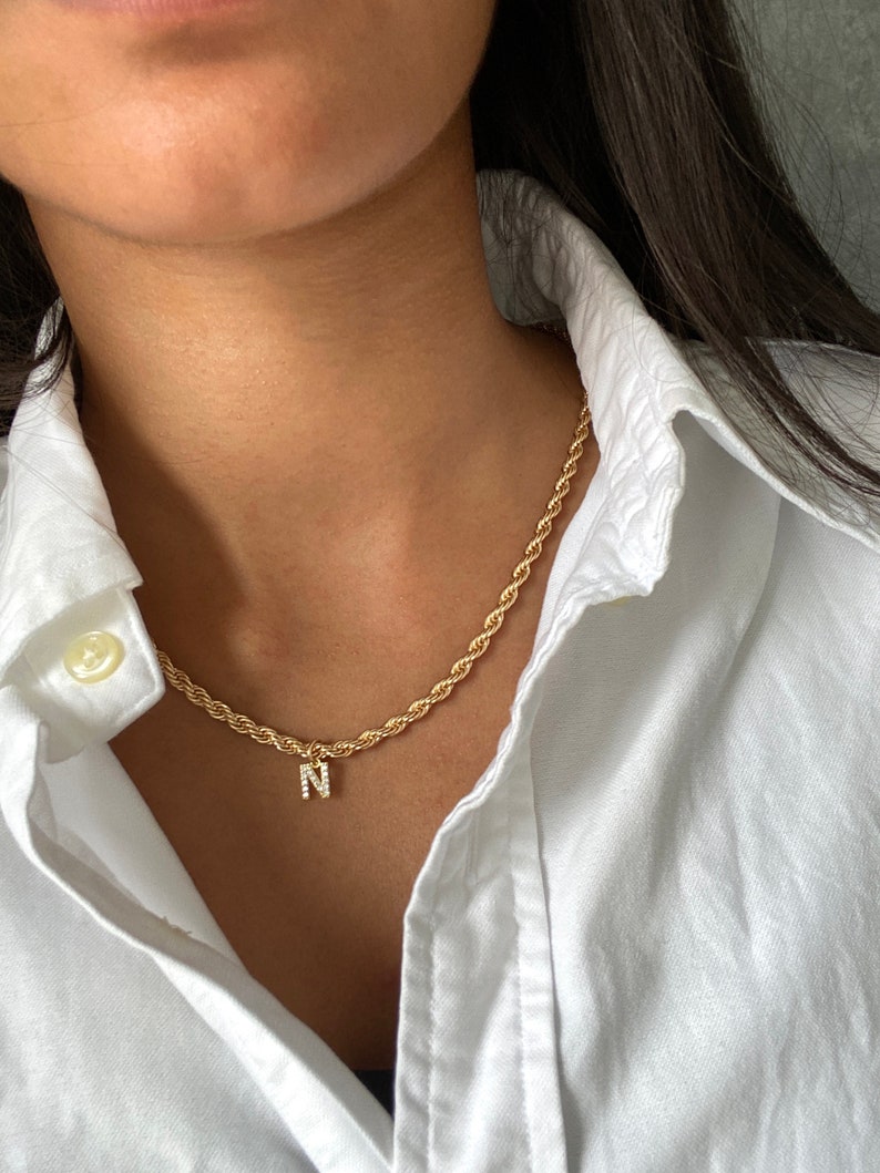 May include: A gold rope chain necklace with a small pendant featuring the letter 'N' encrusted with clear rhinestones.