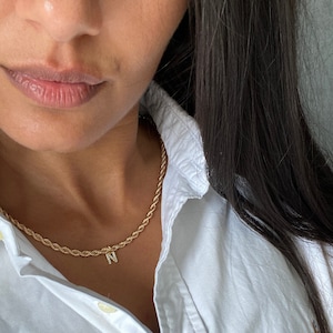May include: A gold rope chain necklace with a small letter 'N' pendant. The pendant is set with small clear stones.