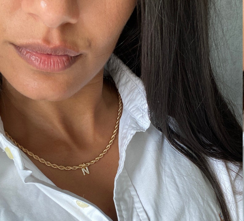 May include: A gold rope chain necklace with a small letter 'N' pendant. The pendant is set with small clear stones.