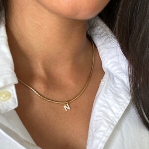 May include: A gold chain necklace with a small pendant in the shape of the letter N, adorned with sparkling clear stones.