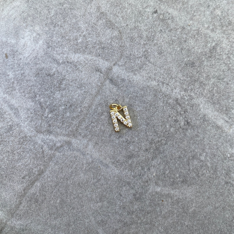 May include: A gold charm in the shape of the letter N, encrusted with small clear rhinestones.