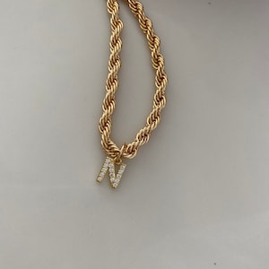 May include: A gold rope chain necklace with a gold letter N pendant encrusted with clear rhinestones.