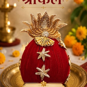 May include: A deep red velvet coconut-shaped object adorned with gold metallic star-shaped appliqués and a large gold lotus-shaped topper. The text "श्रीफल" is printed above, and a label reads "treasure deck by sakshi.." at the base.