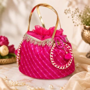 Puede incluir: Un bolso de mano fucsia con cierre de cordón, hecho de tela transparente con rayas plateadas diagonales, un asa metálica dorada y un borde decorativo con perlas blancas. El bolso incluye un cierre fruncido y dos detalles laterales circulares con perlas.