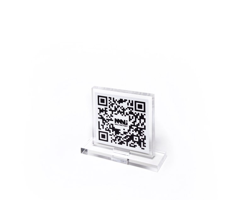 K&ouml;nnte beinhalten: Ein klarer Acryl-Displayst&auml;nder mit einem schwarz-wei&szlig;en QR-Code. Der QR-Code zeigt den Text "NNI WALL FACTORY". Der St&auml;nder ist rechteckig mit einem Sockel und einem Schlitz zur Aufnahme der gedruckten Karte.