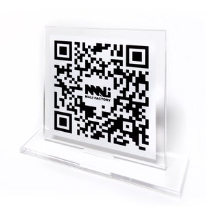 K&ouml;nnte beinhalten: Ein klarer Acryl-Displayst&auml;nder, der eine wei&szlig;e Karte mit einem schwarzen QR-Code und dem Text "MALI FACTORY" h&auml;lt. Der St&auml;nder hat einen rechteckigen Sockel und einen Schlitz, um die Karte aufrecht zu halten. Der Hintergrund ist wei&szlig;.