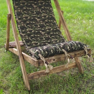 May include: A wooden folding chair with a camouflage patterned fabric seat and back. The chair is sitting on a grassy lawn.