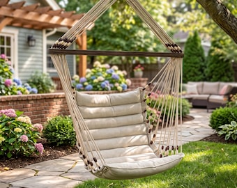 May include: A hanging chair featuring a cream-colored tufted cushion suspended by thick off-white ropes. The ropes are accented with small dark brown wooden beads and attached to a horizontal dark brown wooden spreader bar at the top.