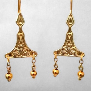 Puede incluir: Un par de pendientes de oro con un dise&ntilde;o triangular y cuentas colgantes. Los pendientes tienen un patr&oacute;n detallado e intrincado.