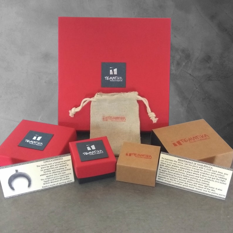 Puede incluir: Un conjunto de embalajes de joyer&iacute;a, que incluye cajas rojas, una peque&ntilde;a bolsa beige y varias cajas de cart&oacute;n. Las cajas presentan el logotipo "TEMATIKA". Las tarjetas describen los "LUNULA EARRINGS" y el mantenimiento de las joyas.