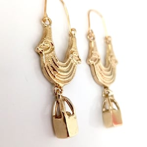 May include: Gold hoop earrings with a detailed design and a dangling square charm.