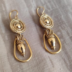May include: A pair of gold-tone dangle earrings with a round, textured disc and a teardrop-shaped pendant.
