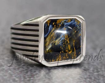 May include: A silver ring with a square blue and gold tiger's eye gemstone. The ring has a striped band.