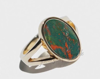 May include: A gold ring with a green and orange oval-shaped stone set in a bezel setting. The ring has a split shank.